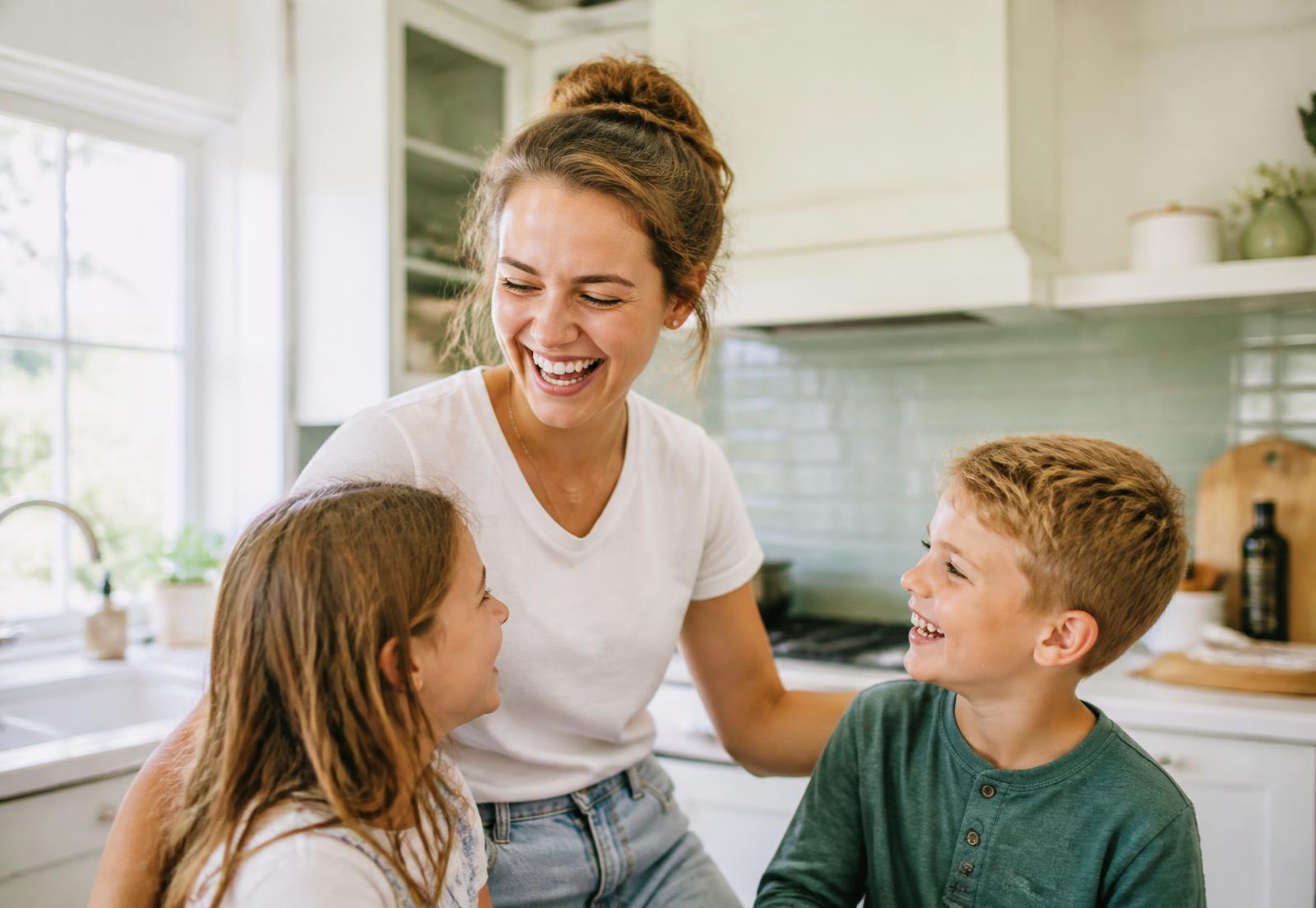 An au pair laughing with two children in a bright kitchen
